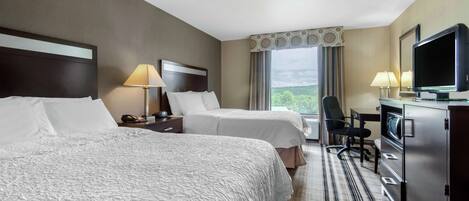 A hotel room with two beds, a desk with a television, a chair, and a dresser.