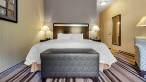 A hotel room with a large bed, two bedside lamps, a headboard, a bench, a mirror, and a door. - Hampton Inn Meadville (Meadville)