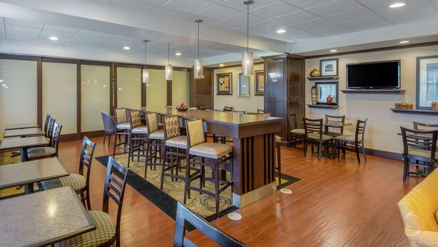 A hotel lobby with multiple dining tables and chairs, a central bar area, and a flat-screen TV mounted on the wall. - Hampton Inn Meadville (Meadville)