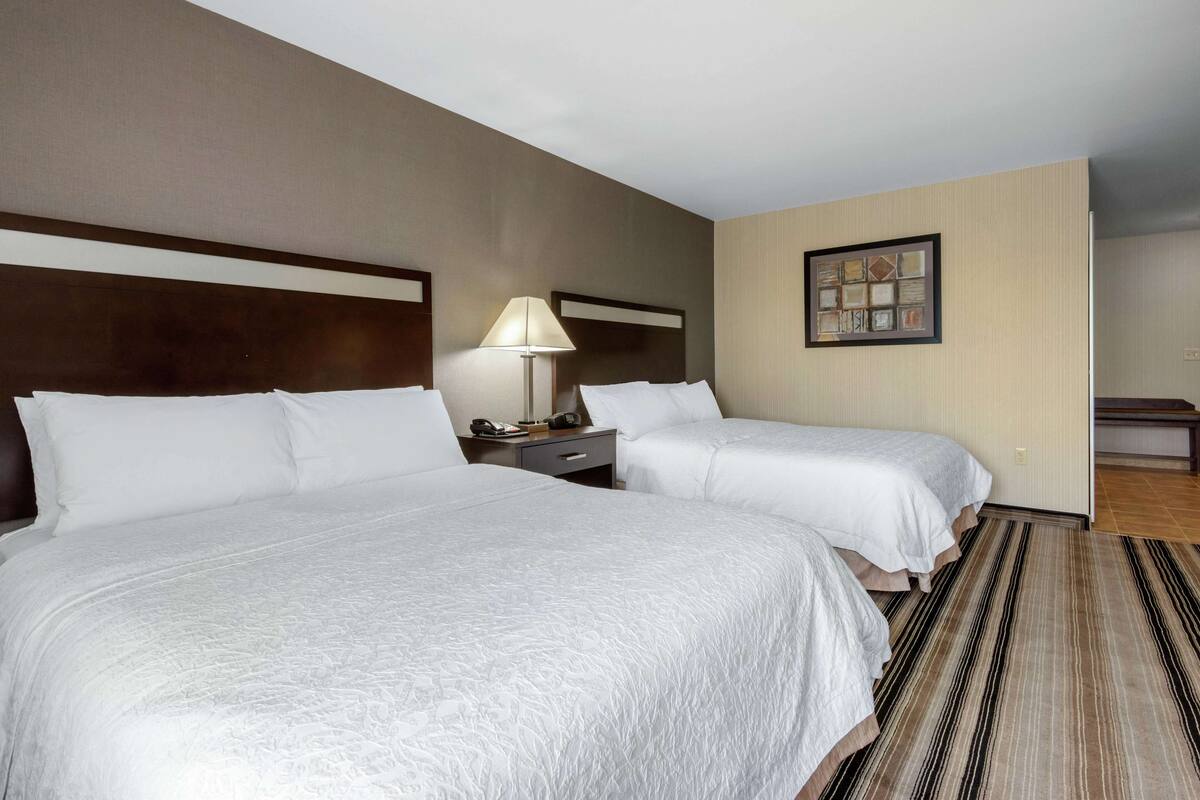 Una habitación de hotel con dos camas, una mesita de noche, una lámpara y un cuadro en la pared.