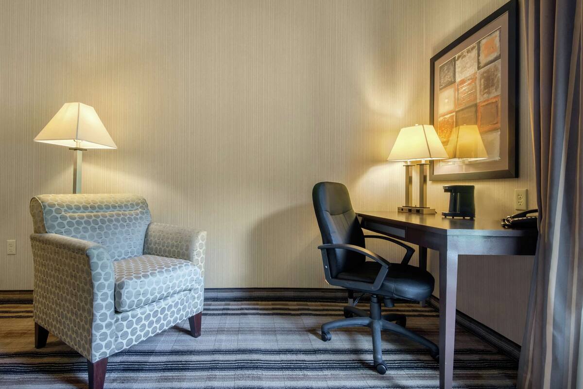 Habitación de hotel con un sillón estampado, una silla de oficina negra, un escritorio y dos lámparas de pared.