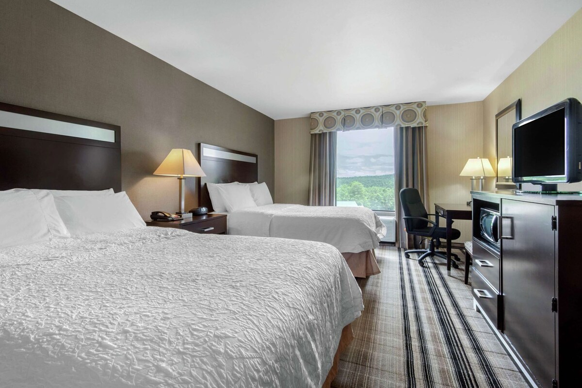 Quarto de hotel com duas camas, uma escrivaninha, televisão e vista para o exterior.