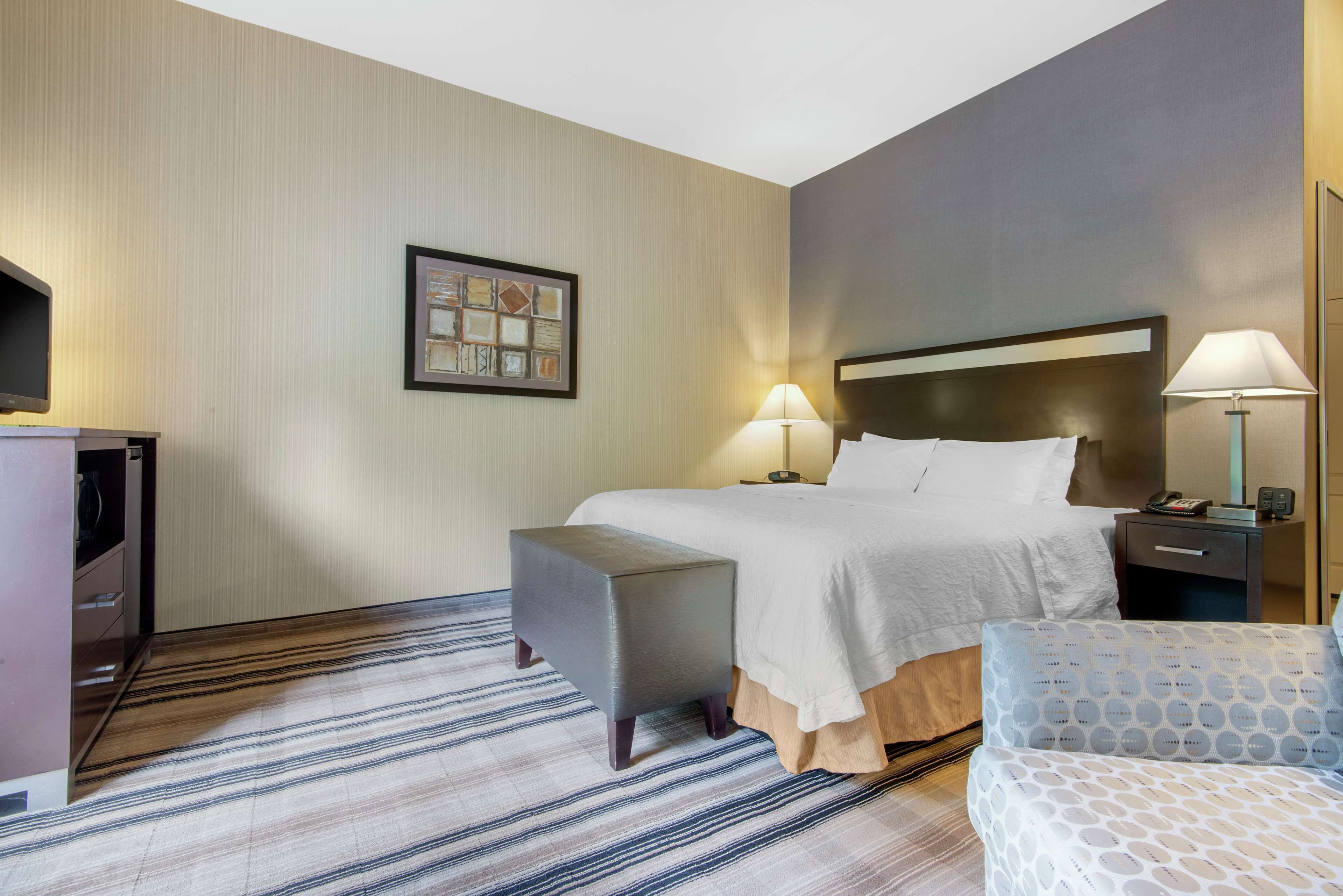A hotel room with a bed, bedside tables, a desk, a chair, and a patterned carpet.
