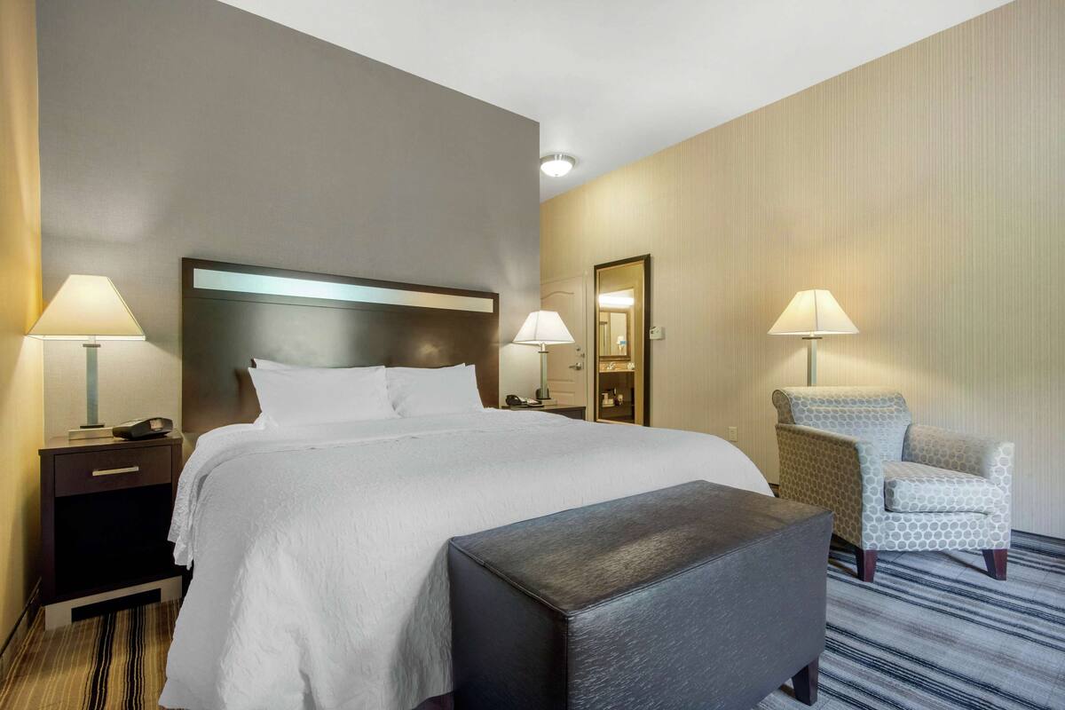 Habitación de hotel con una cama grande, dos mesitas de noche con lámparas, una silla y una pequeña mesa.