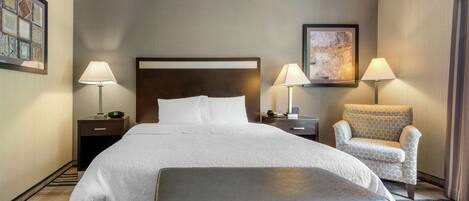 A hotel room with a large bed, two bedside tables, a chair, and a bench.