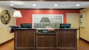 A reception desk with two computers, a clock, and a framed picture of a beach scene.