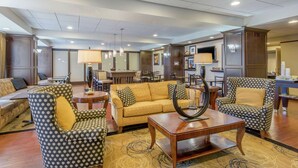 A hotel lobby with a sofa, armchairs, a coffee table, and a dining area. - Hampton Inn Meadville (Meadville)