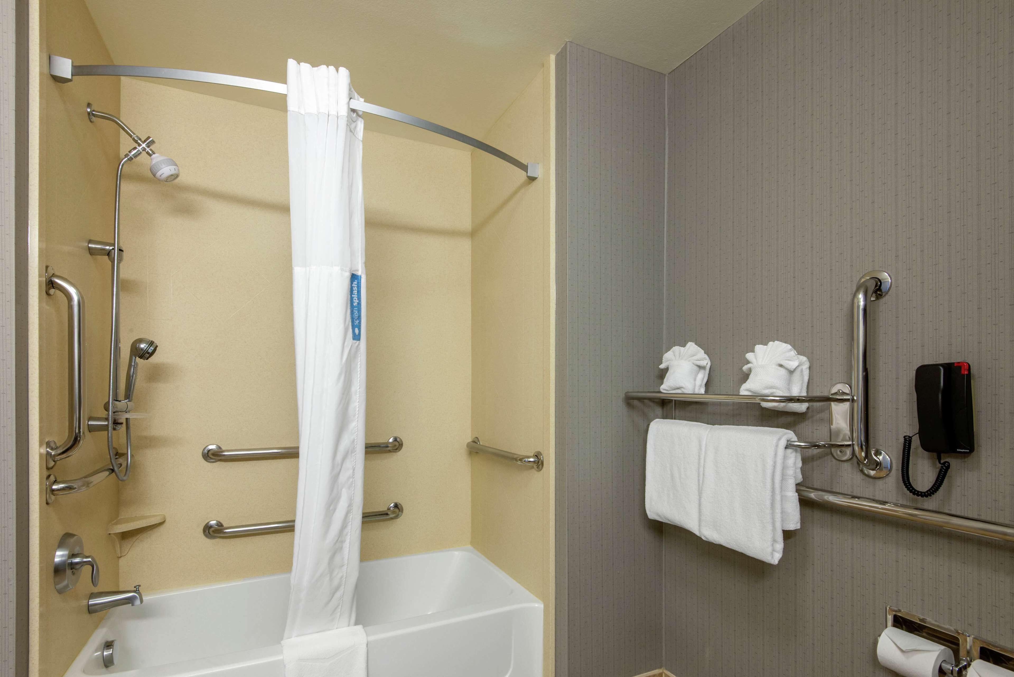 A bathroom with a bathtub, grab bars, a shower, a towel rack, and a telephone.