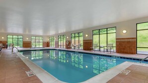 A large indoor swimming pool with clear glass walls, tiled floor, and several lounge chairs along the poolside. - Hampton Inn Meadville (Meadville)
