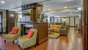 A lobby with a fireplace, patterned armchairs, a sofa, and a dining area. - Hampton Inn Meadville (Meadville)