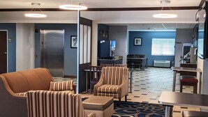 A hotel lobby with striped armchairs, a sofa, a dining area, and a kitchenette.