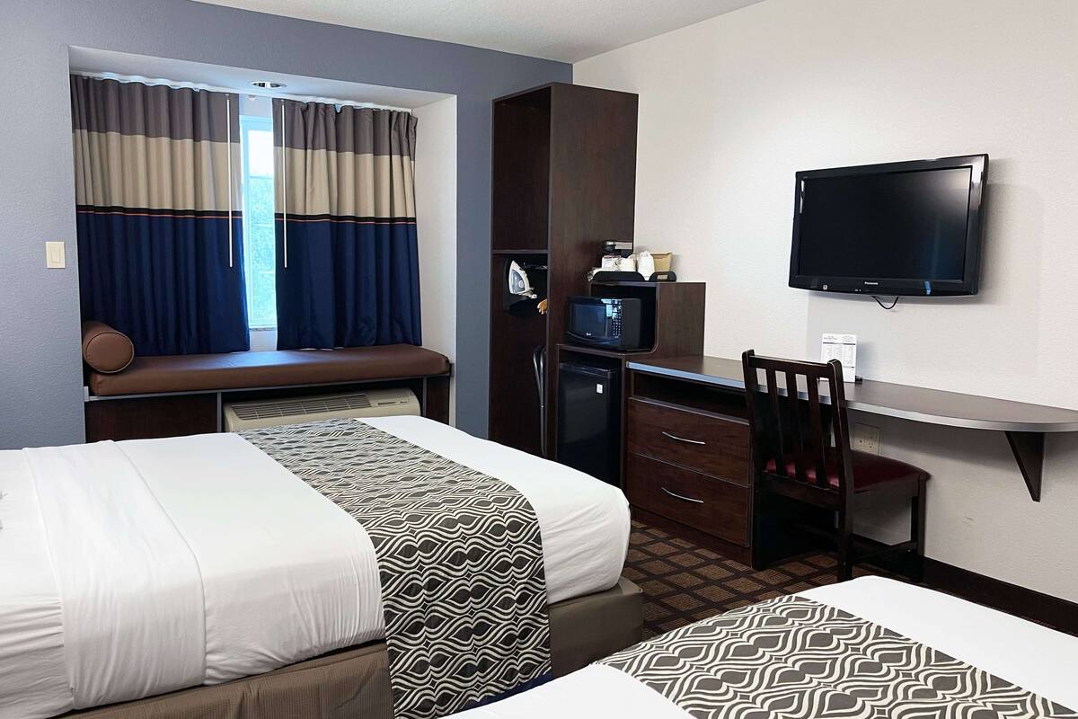 A hotel room with two beds, a desk with a chair, a television, and a window with curtains.