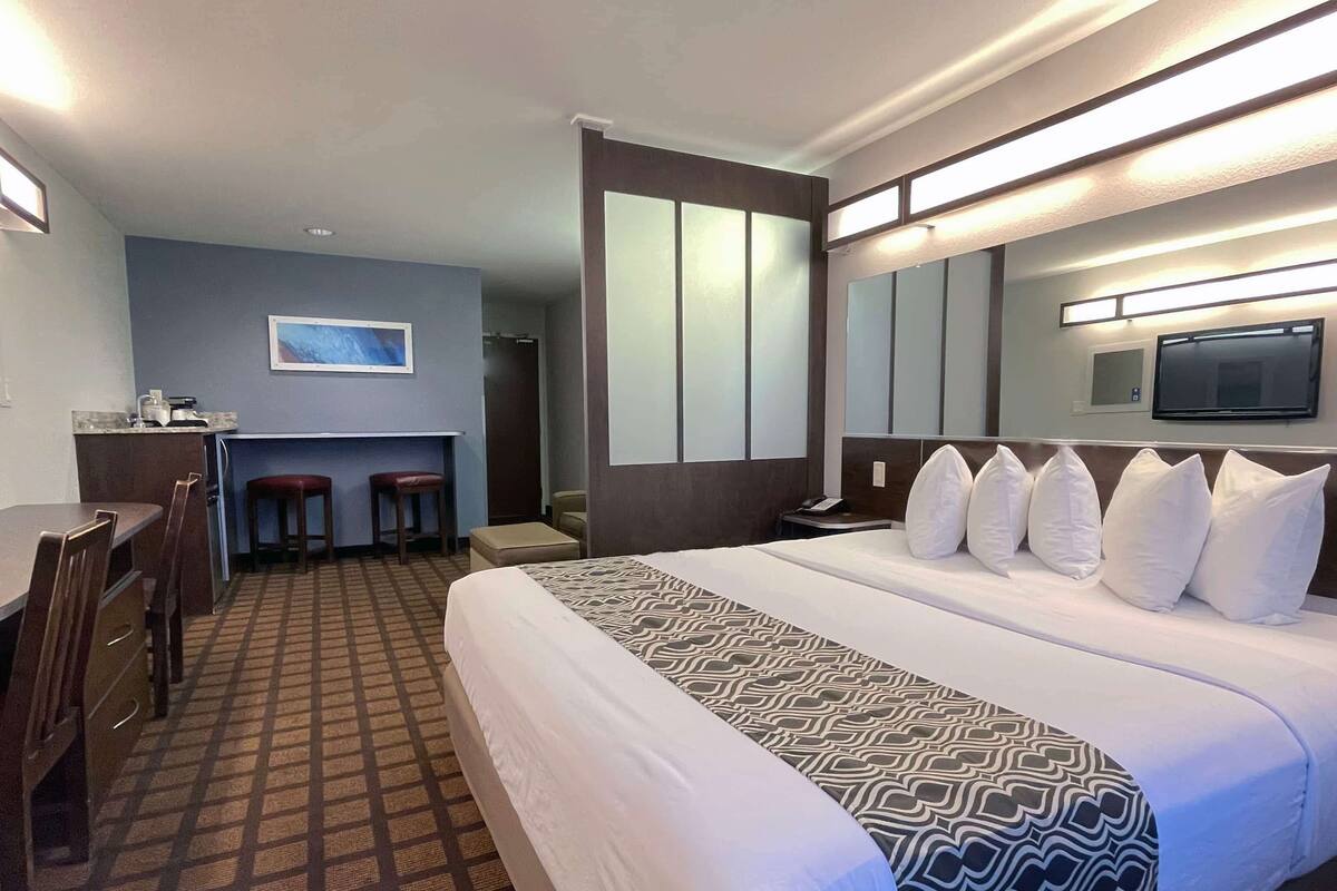 A hotel room with a large bed, a desk, two chairs, a small table, and a television.