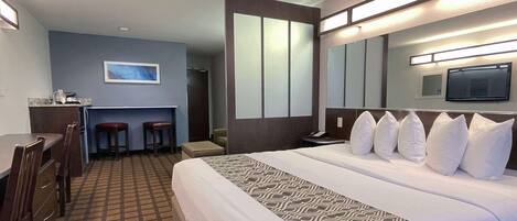 A hotel room with a large bed, a desk, two chairs, a small table, and a television.