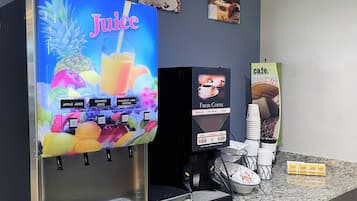 En juiceautomat med möjlighet att välja mellan äppel-, apelsin- och tranbärsjuice, en kaffemaskin som brygger färskt kaffe och en skylt som visar att det är ett café.