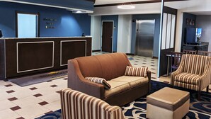 A hotel lobby with a reception desk, a sofa, striped armchairs, and a small ottoman.