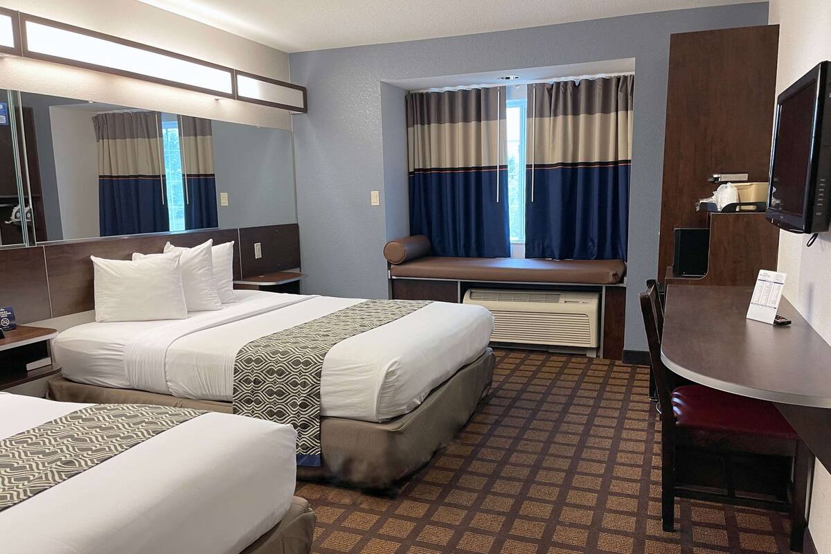 A hotel room with two beds, a desk, a television, and a window with curtains.