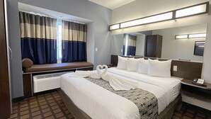 A hotel room with a large bed, a bench by the window, a bedside table with a phone, and a mirror above the bed.