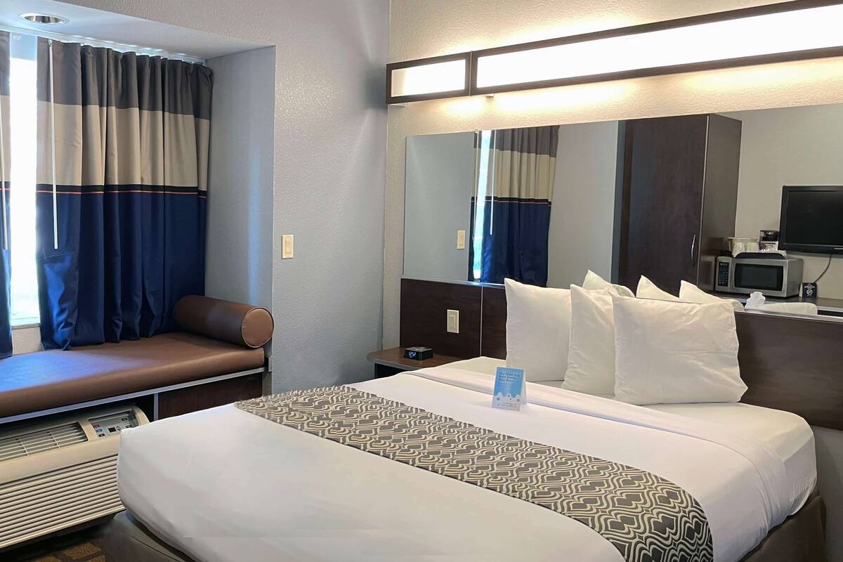 A hotel room with a bed, a seating area, a desk with a computer, and a television.