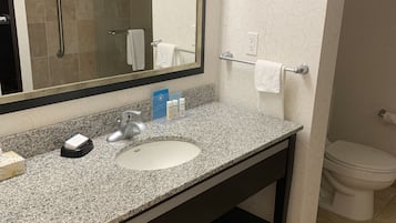 Un baño con lavamanos de encimera de granito, un espejo, toallero y un inodoro.