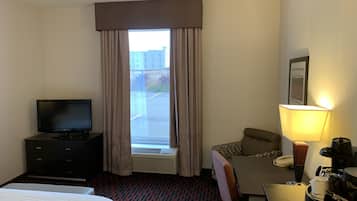 Una camera d'albergo con un letto, una scrivania con una lampada, una televisione, un divano e una finestra con tende.