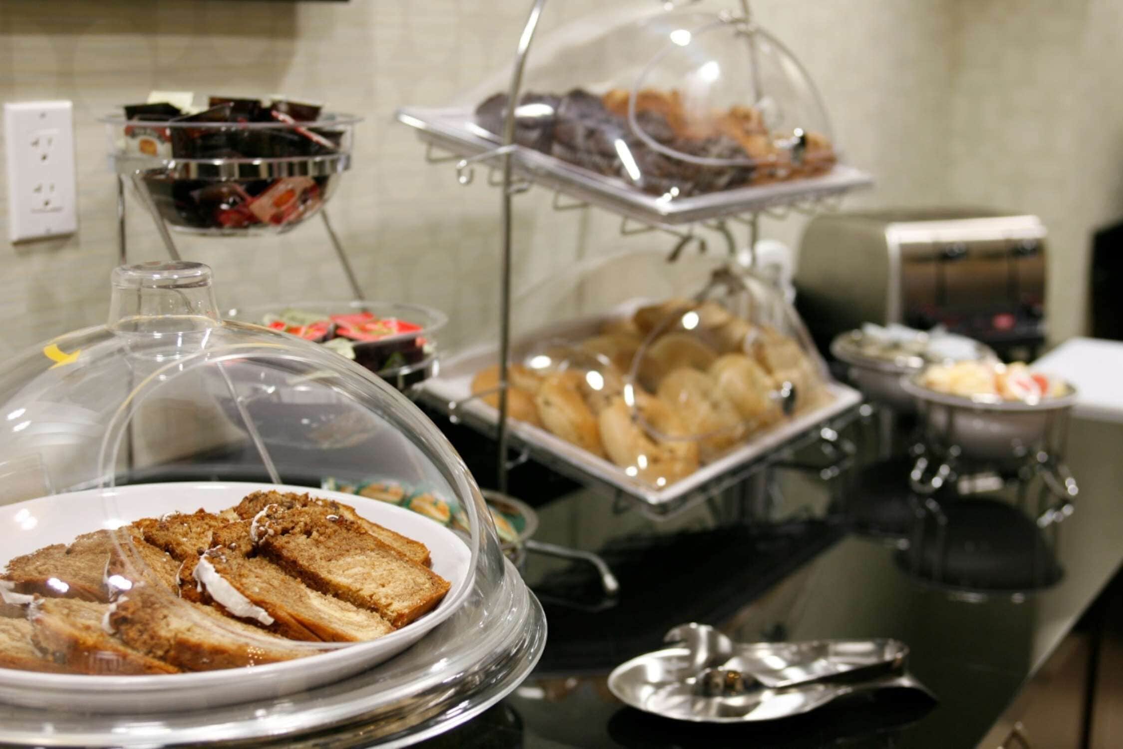 A buffet with various food items displayed under glass covers, including bread and pastries.