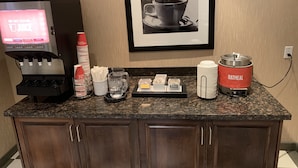 Un área de cocina con una cafetera, un cuadro en la pared y una máquina para hacer café etiquetada como 'OATMEAL'.