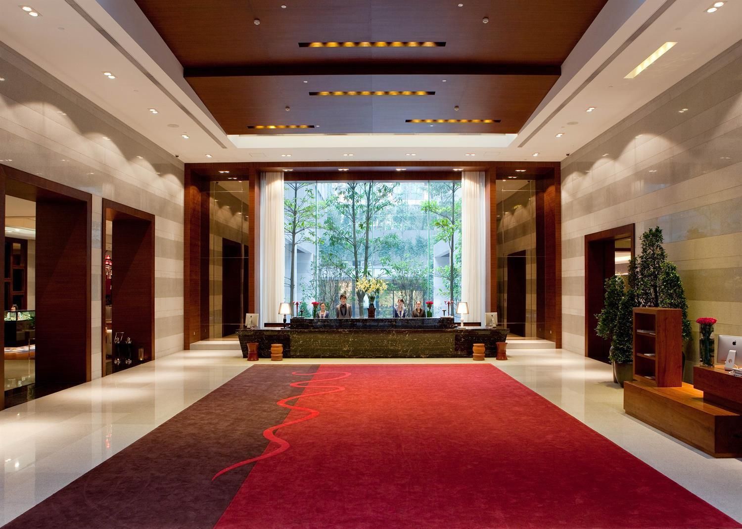 A hotel lobby with a red carpet, a reception desk, and a view of greenery outside.