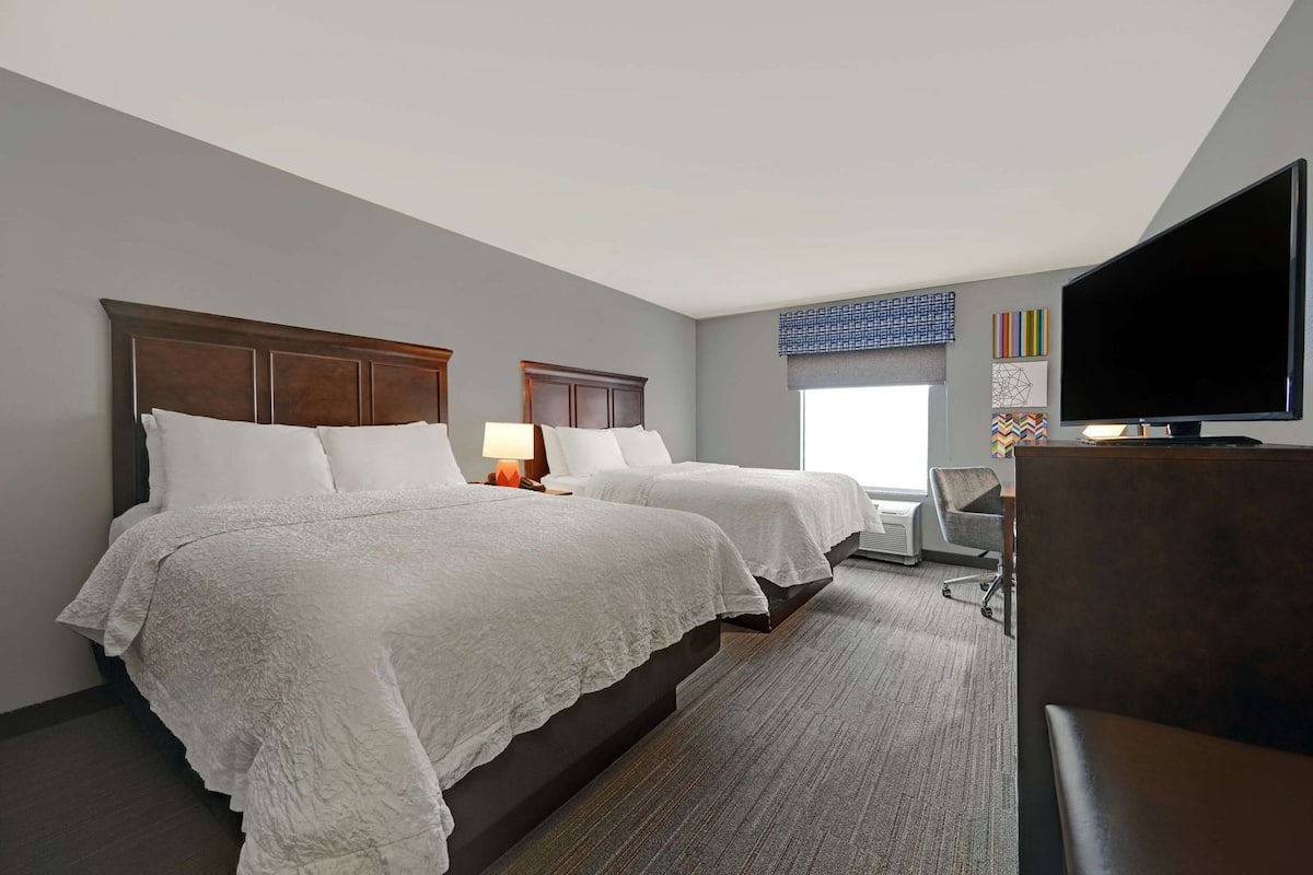 A hotel room with two beds, a TV, a desk, and a chair.