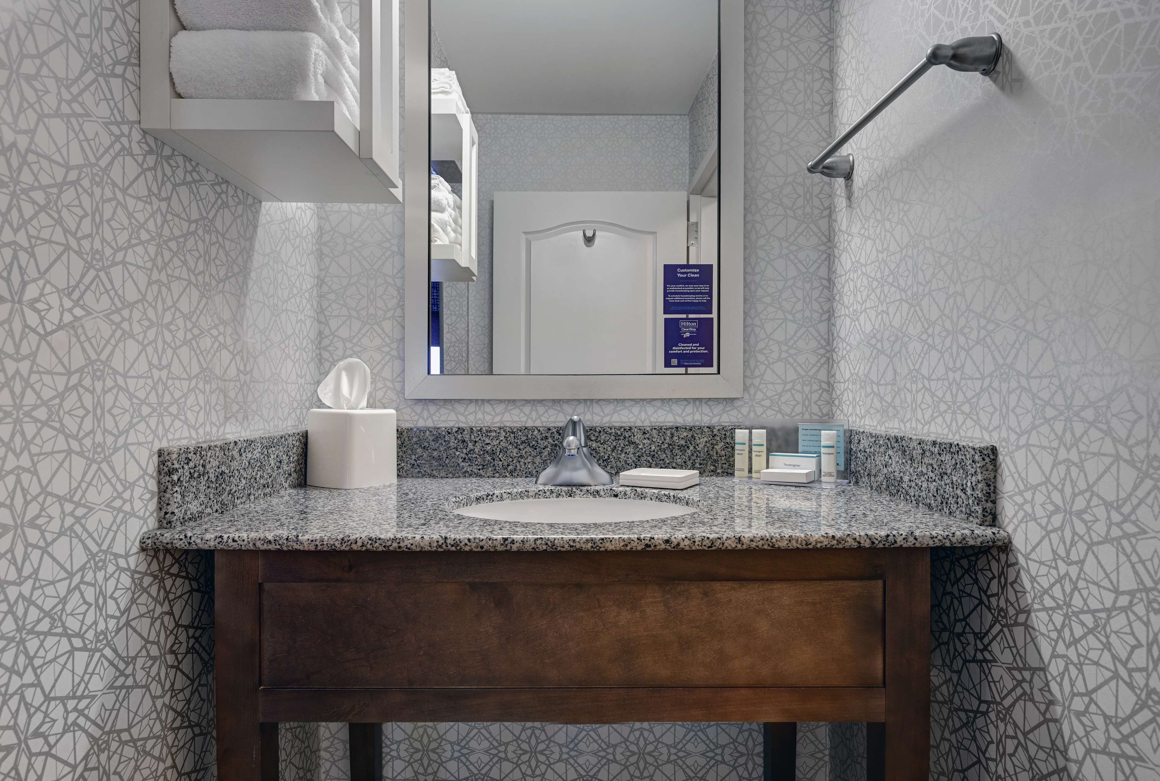 Une salle de bain dotée d’un comptoir en granit, d’un meuble-lavabo en bois, d’un miroir et d’un porte-serviettes.