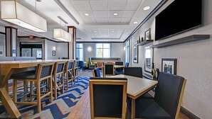 A modern hotel lobby with multiple seating areas, a large flat-screen TV mounted on the wall, and a visible exit sign. - Hampton Inn Farmington (Farmington)
