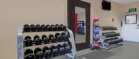 Une salle de sport équipée de matériel de musculation, notamment des haltères et un porte-poids, et un panneau de signalisation indiquant la sortie sur le mur.