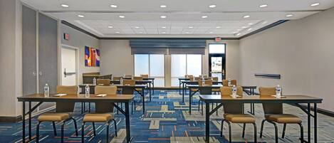 A conference room with tables and chairs, a patterned carpet, and a view of the outside through large windows.