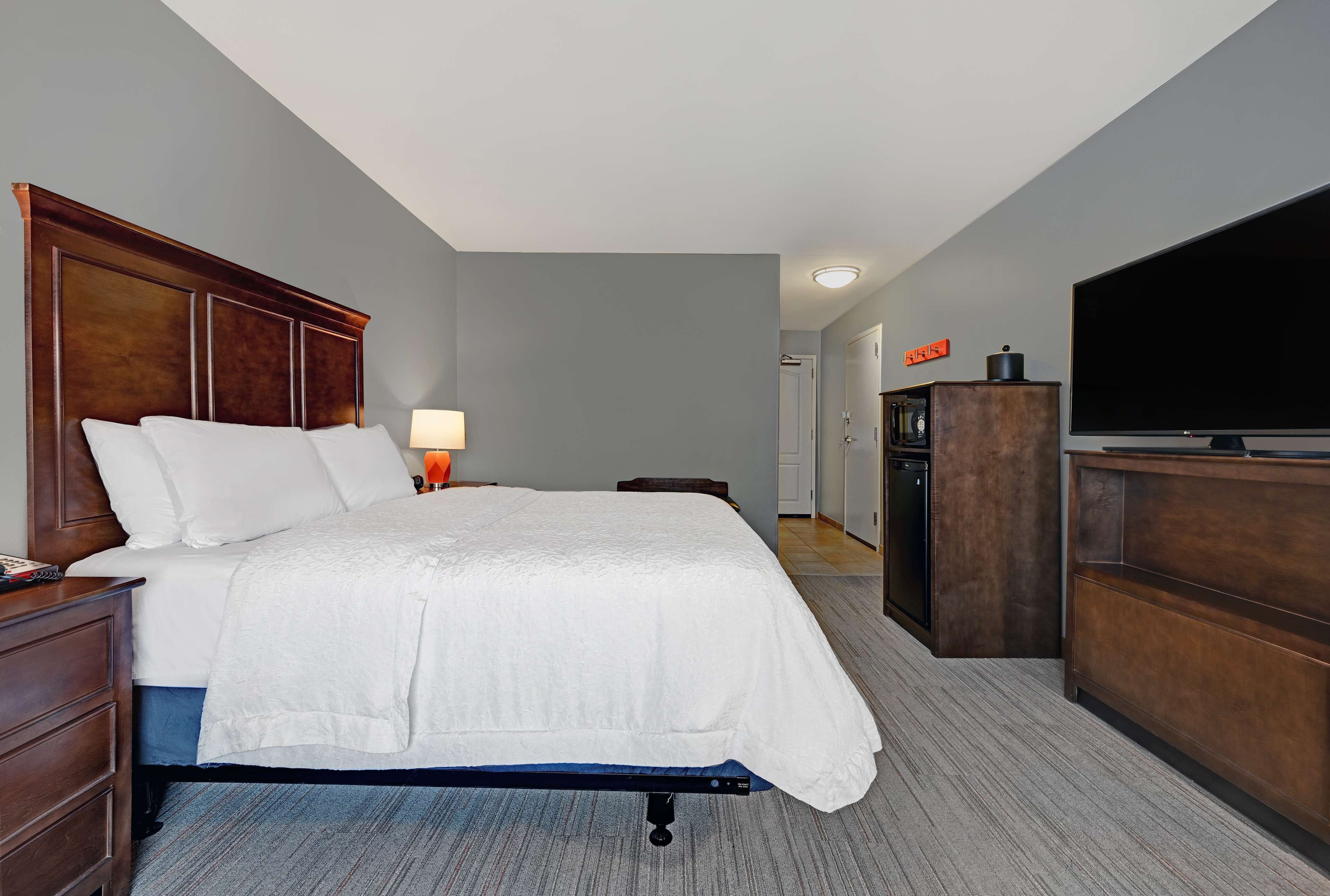 A hotel room with a bed, a desk, a dresser, a television, and a door leading to a bathroom.