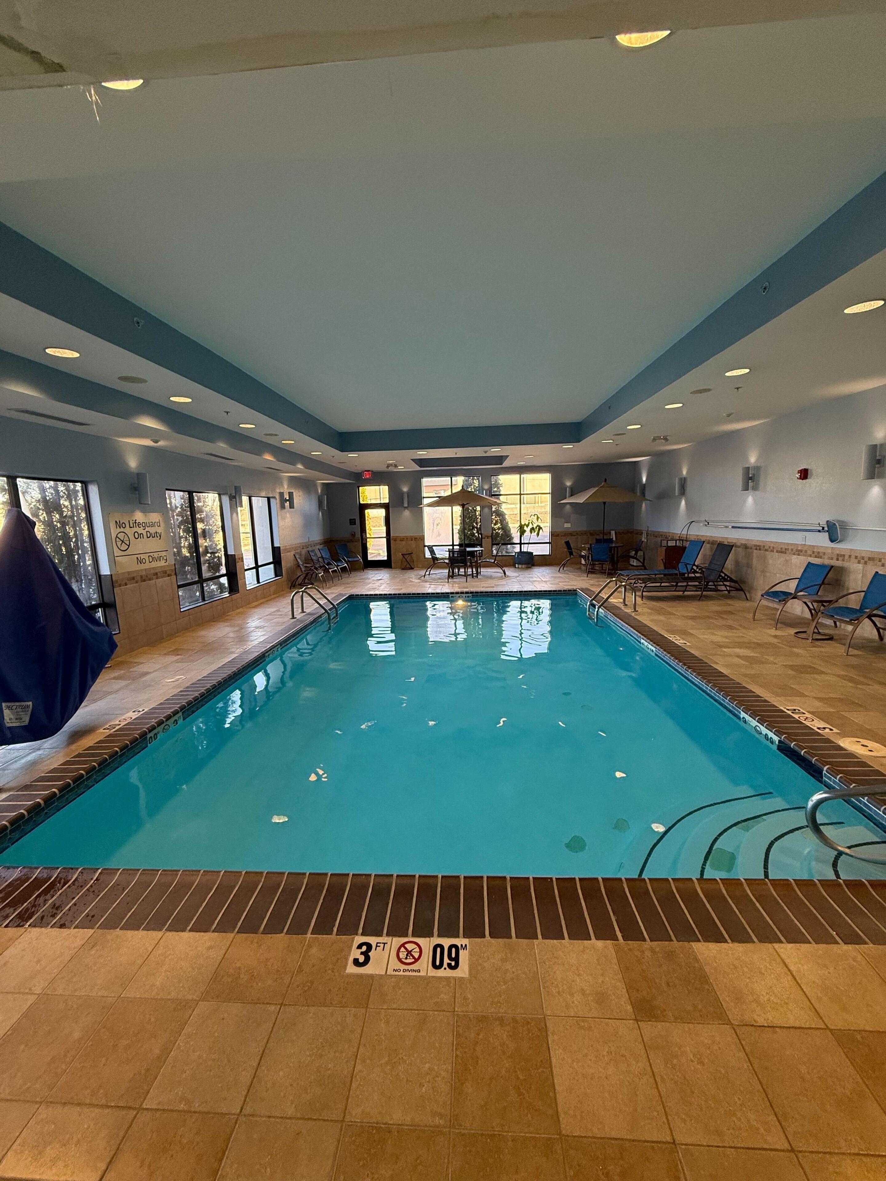 An indoor swimming pool with clear lane markings, a lifeguard chair, and a no diving sign.