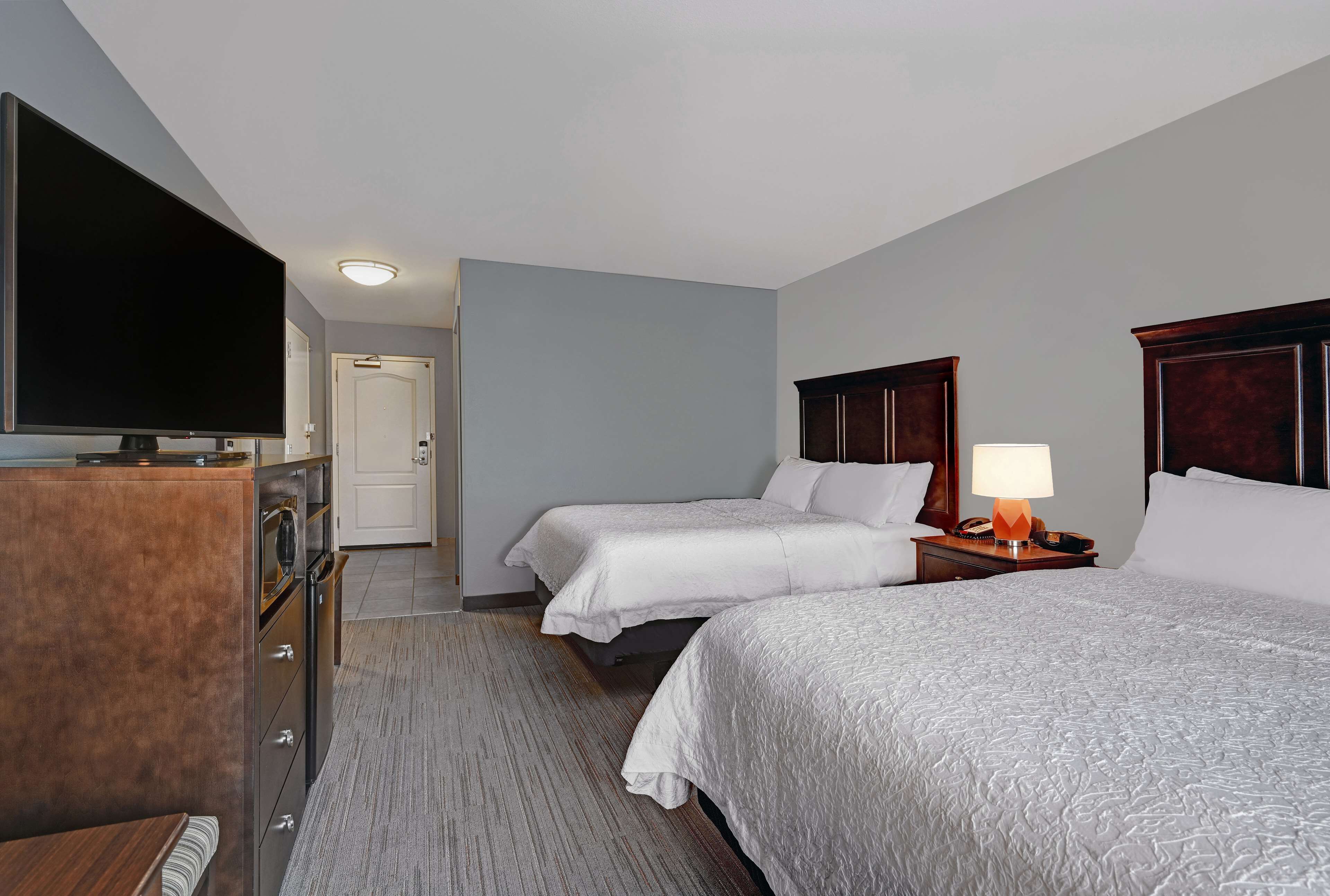 A hotel room with two beds, a TV, a desk with a lamp, and a dresser.