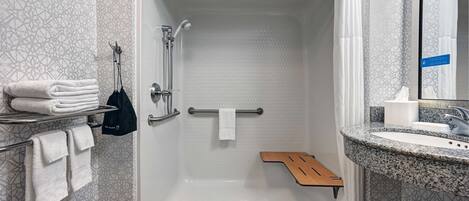 A modern bathroom with a walk-in shower, a hand dryer, a towel rack, and a sink with a granite countertop.