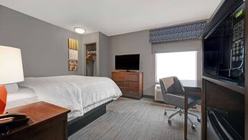 A hotel room with a bed, a desk, a chair, a TV, a dresser, and a microwave.