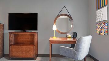 Een hotelkamer met een flatscreen televisie, een houten bureau, een stoel en een spiegel.