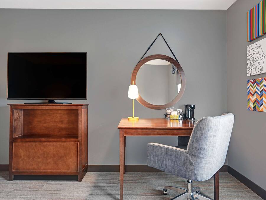 Een hotelkamer met een flatscreen televisie, een houten bureau, een stoel en een spiegel.