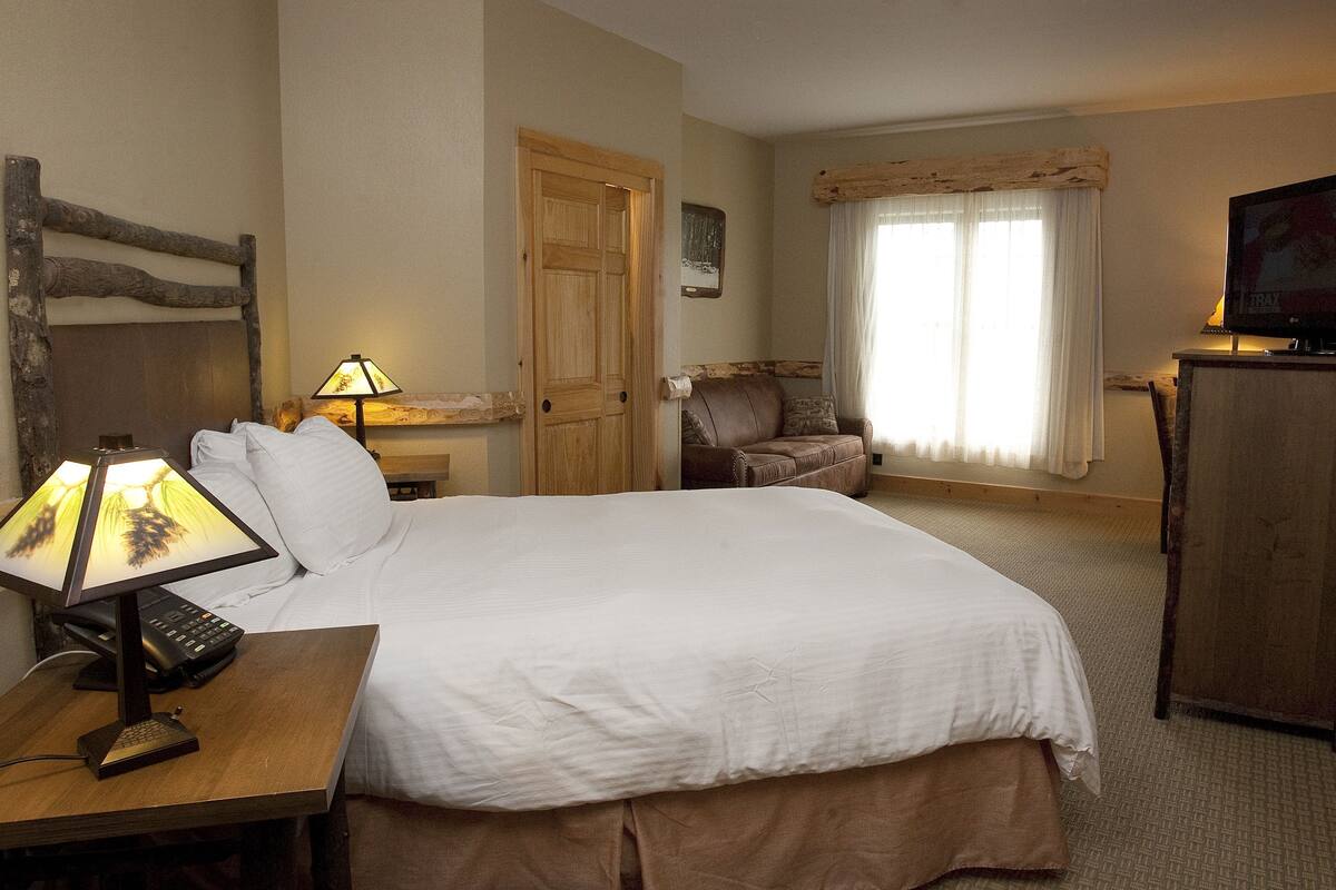 A hotel room with a bed, a desk with a lamp, a chair, a television, and a wooden headboard.