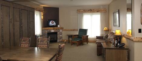 Un salón amplio con una mesa de comedor de madera, asientos cómodos, una chimenea y una televisión.
