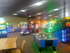 Un salón de juegos interior con varias máquinas de juego, una mesa de billar y zonas de estar.