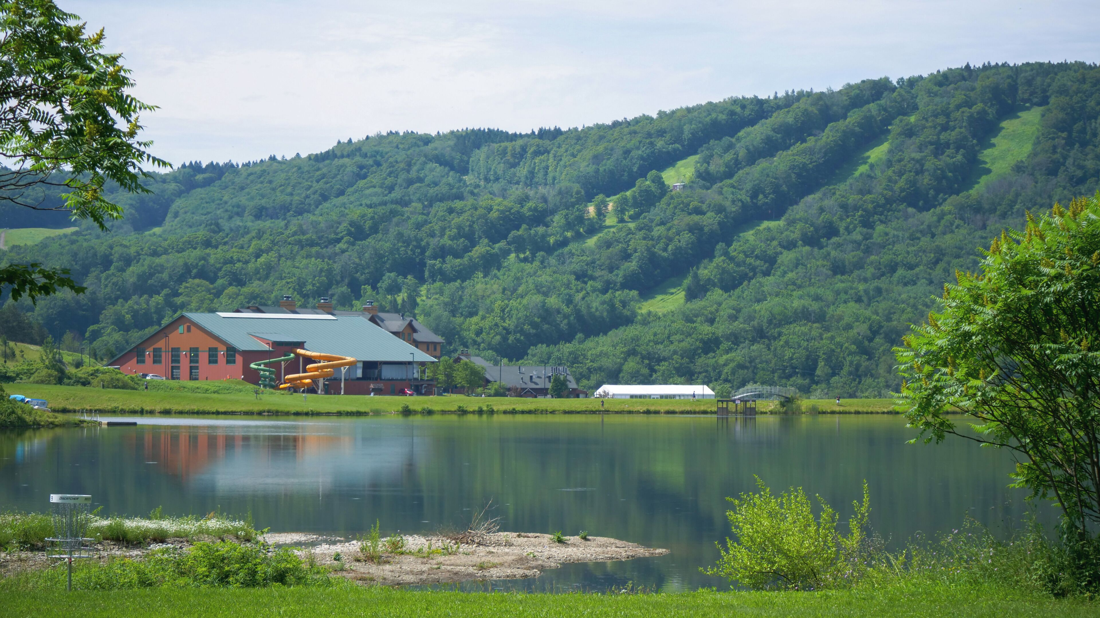 A lakeside view with a red building, a playground, and a white barn.
