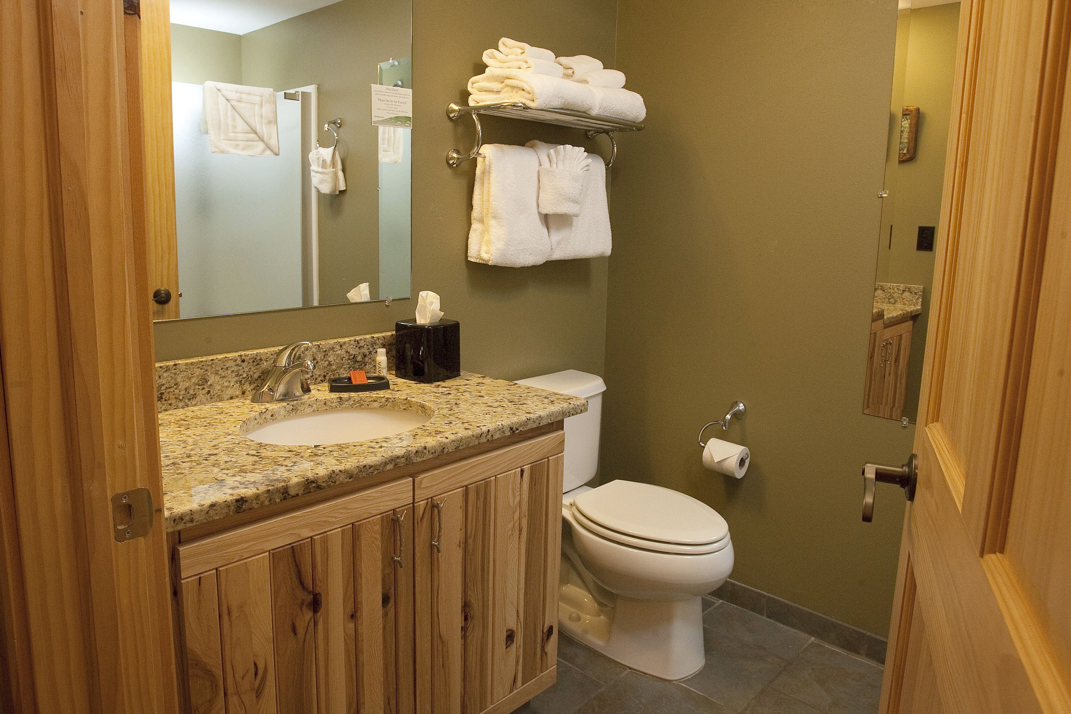 A bathroom with a wooden vanity, a sink, a toilet, and a towel rack with folded towels.