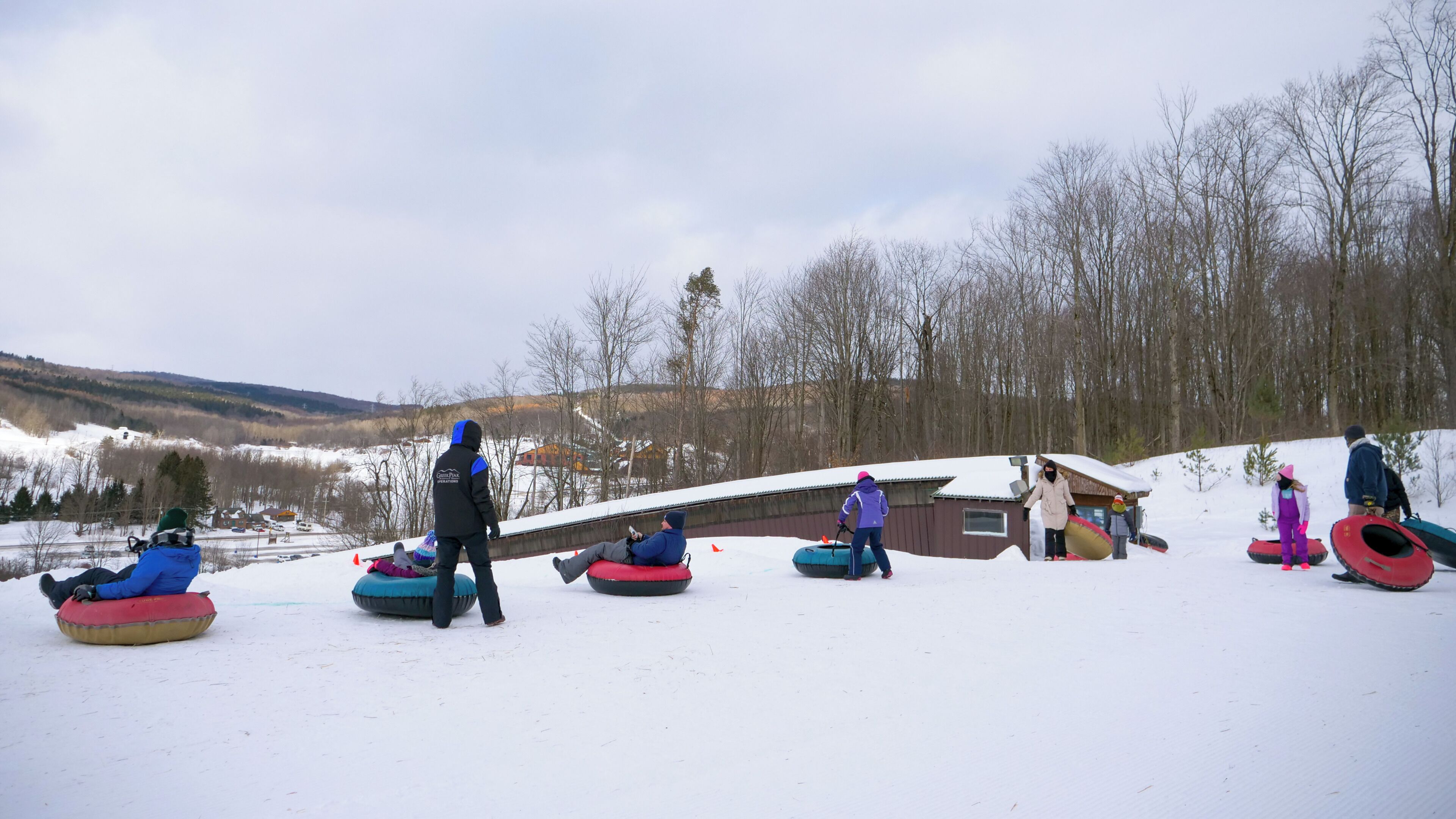 A snowy landscape with people preparing for snow tubing.