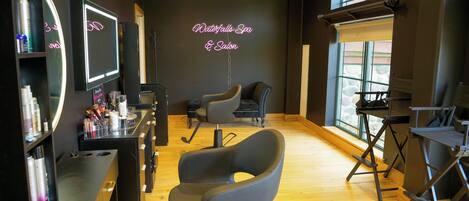 L’intérieur d’un salon de beauté, avec un plancher en bois, des fauteuils noirs et gris, un miroir et un panneau néon indiquant « Waterfalls Spa & Salon ».