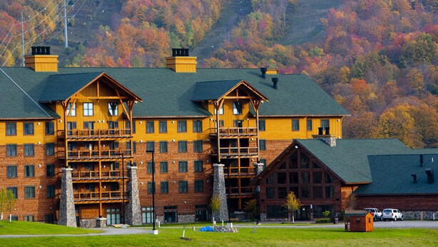 A large lodge with multiple stories, a prominent wooden facade, and a scenic mountain backdrop.