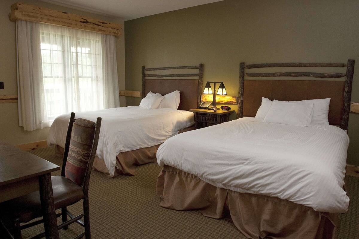 A hotel room with two beds, a desk, and a chair.