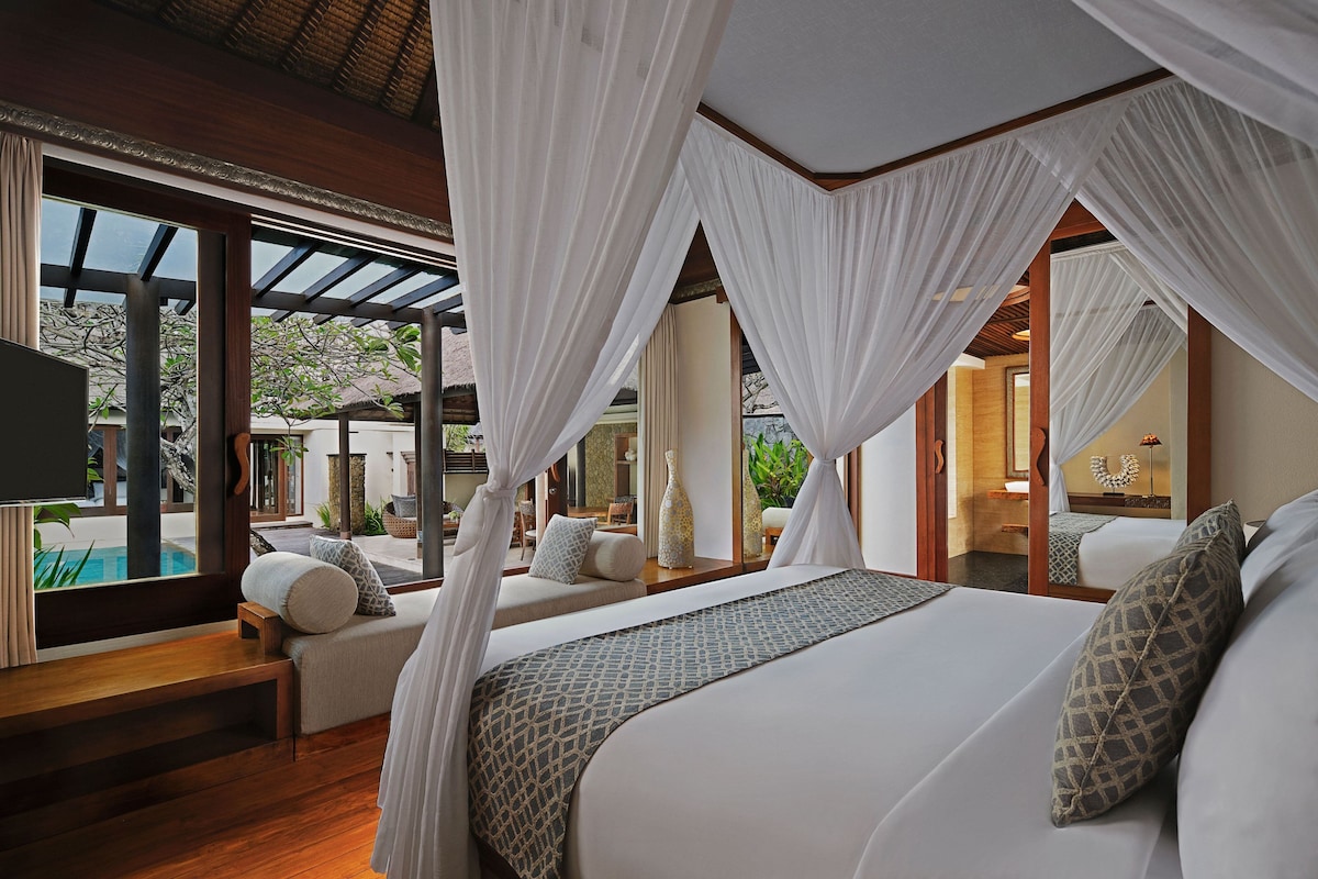 Ein Schlafzimmer mit einem großen Bett, einer Sitzecke und Blick auf einen Pool.